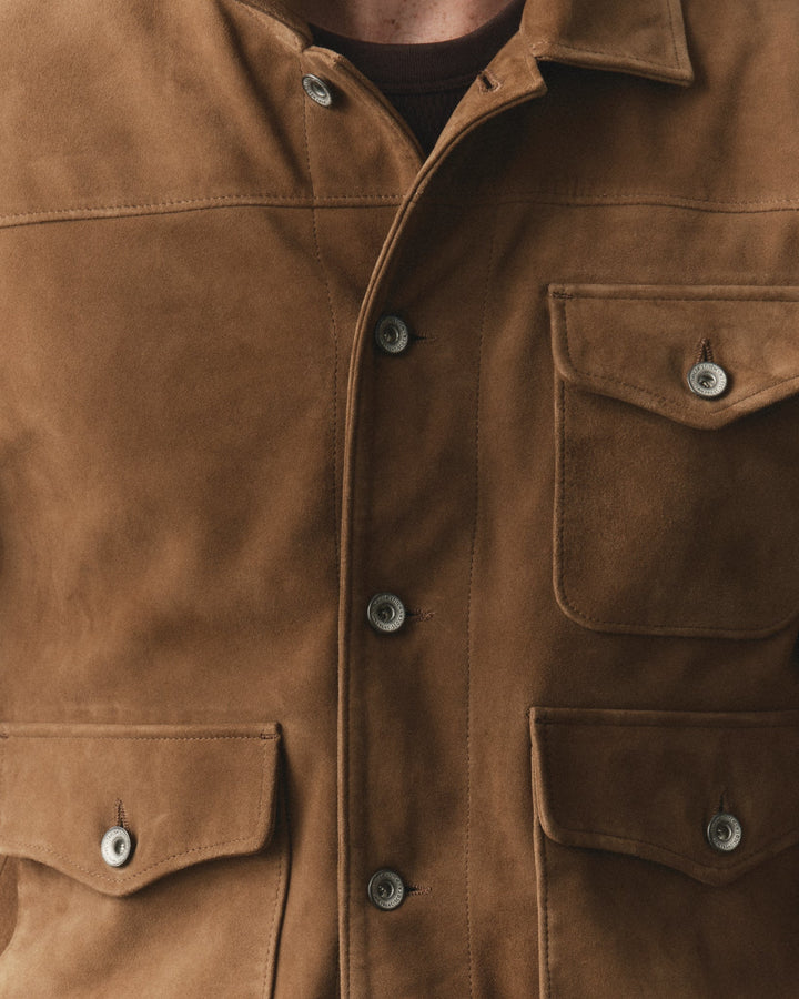 Close-up of a brown suede jacket with silver-toned metal buttons, featuring a collar, button-front closure, and two chest flap pockets.