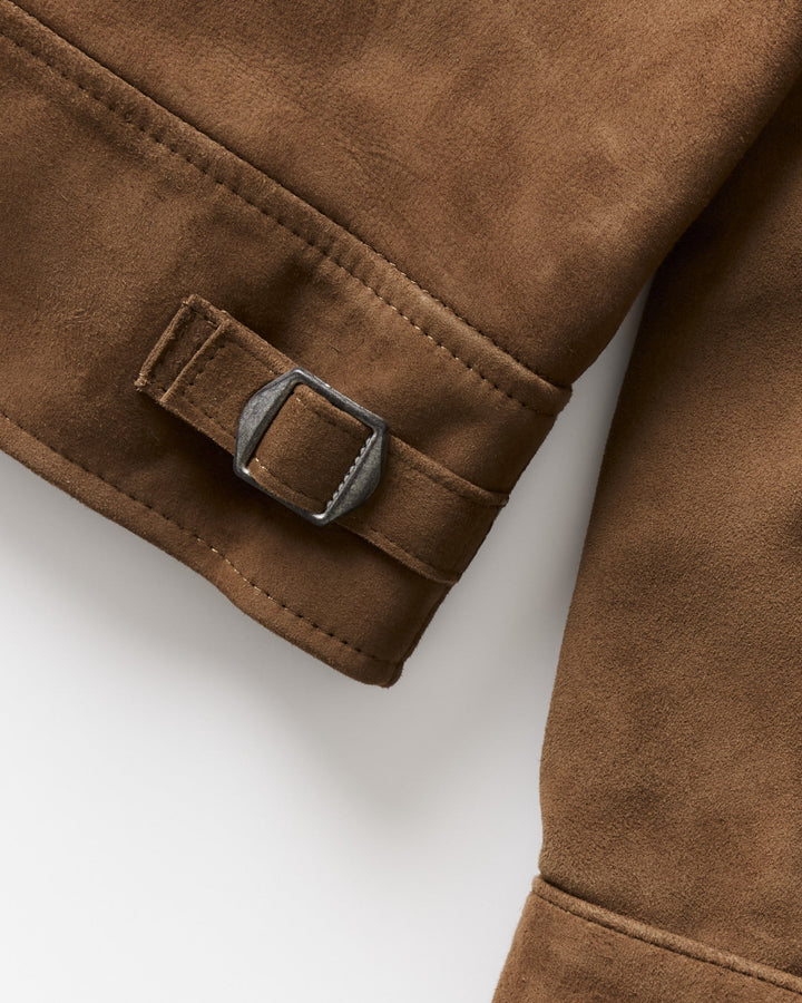 Close-up of a brown suede or nubuck jacket sleeve with a matching fabric tab and a dark metal buckle, shown on a light gray background.