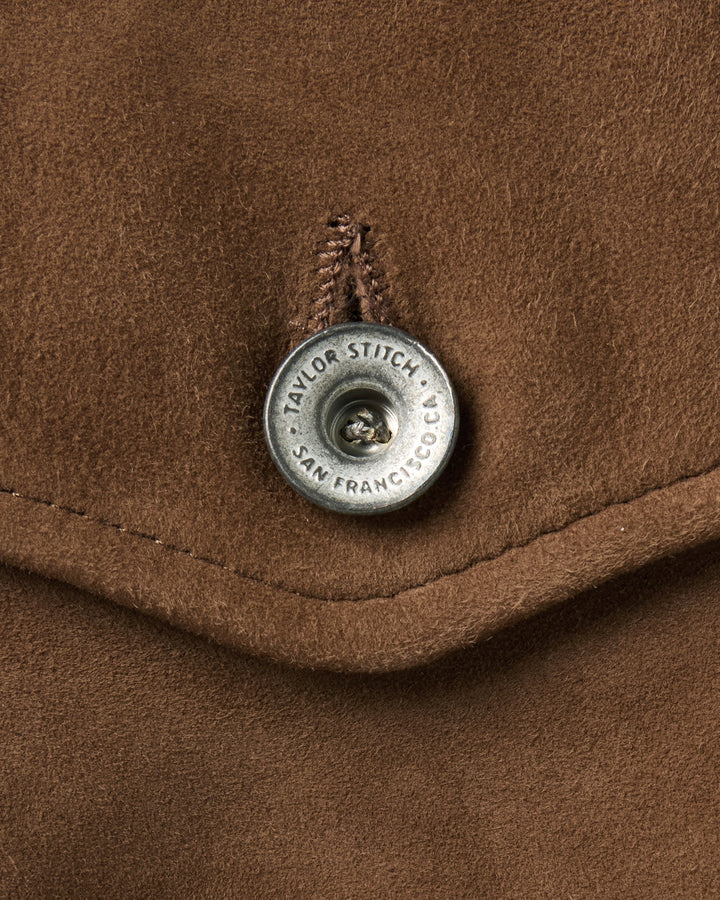 Close-up of a brown suede jacket detail featuring a silver metal button with &