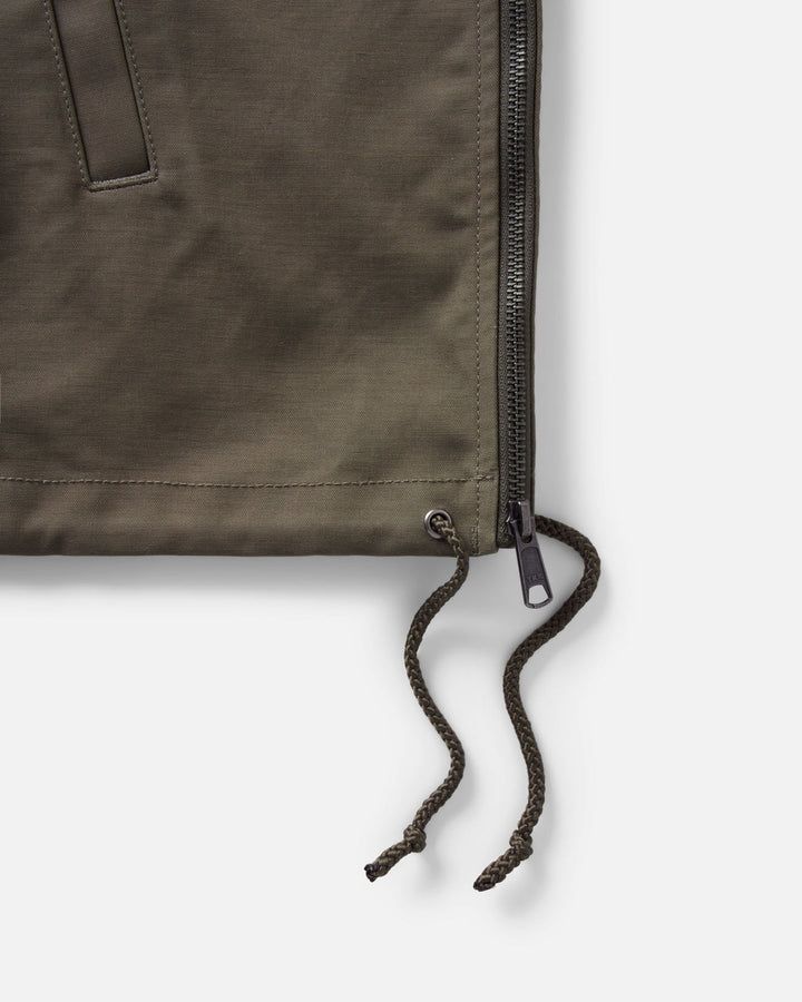 Close-up of an olive green hatteras anorak jacket showing a black zipper, drawstring cord, and metal hardware against a light gray background.