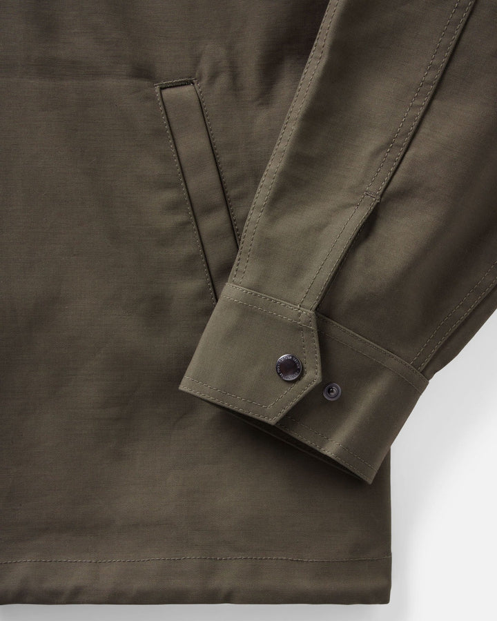 Close-up of an olive green Hatteras anorak jacket showing the sleeve cuff with button tabs and a side pocket seam, photographed on a clean white background.