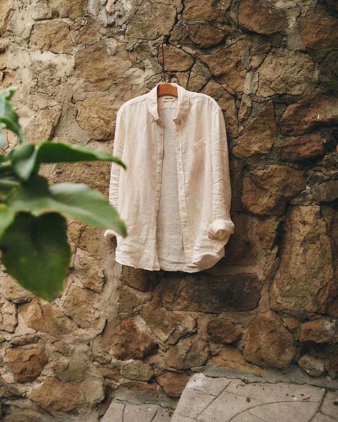 Vintage White shirt hanging on a wooden hanger against a stone wall.