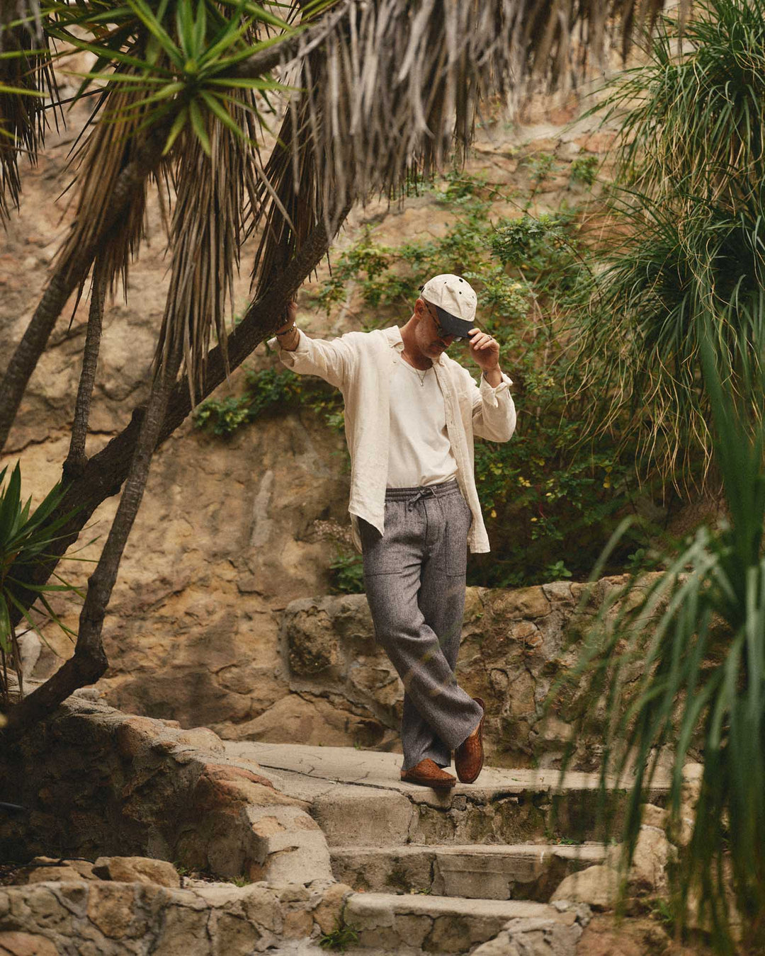 Man wearing the Jack Shirt in Vintage White walking up stone steps in a tropical setting with plants and rocks.