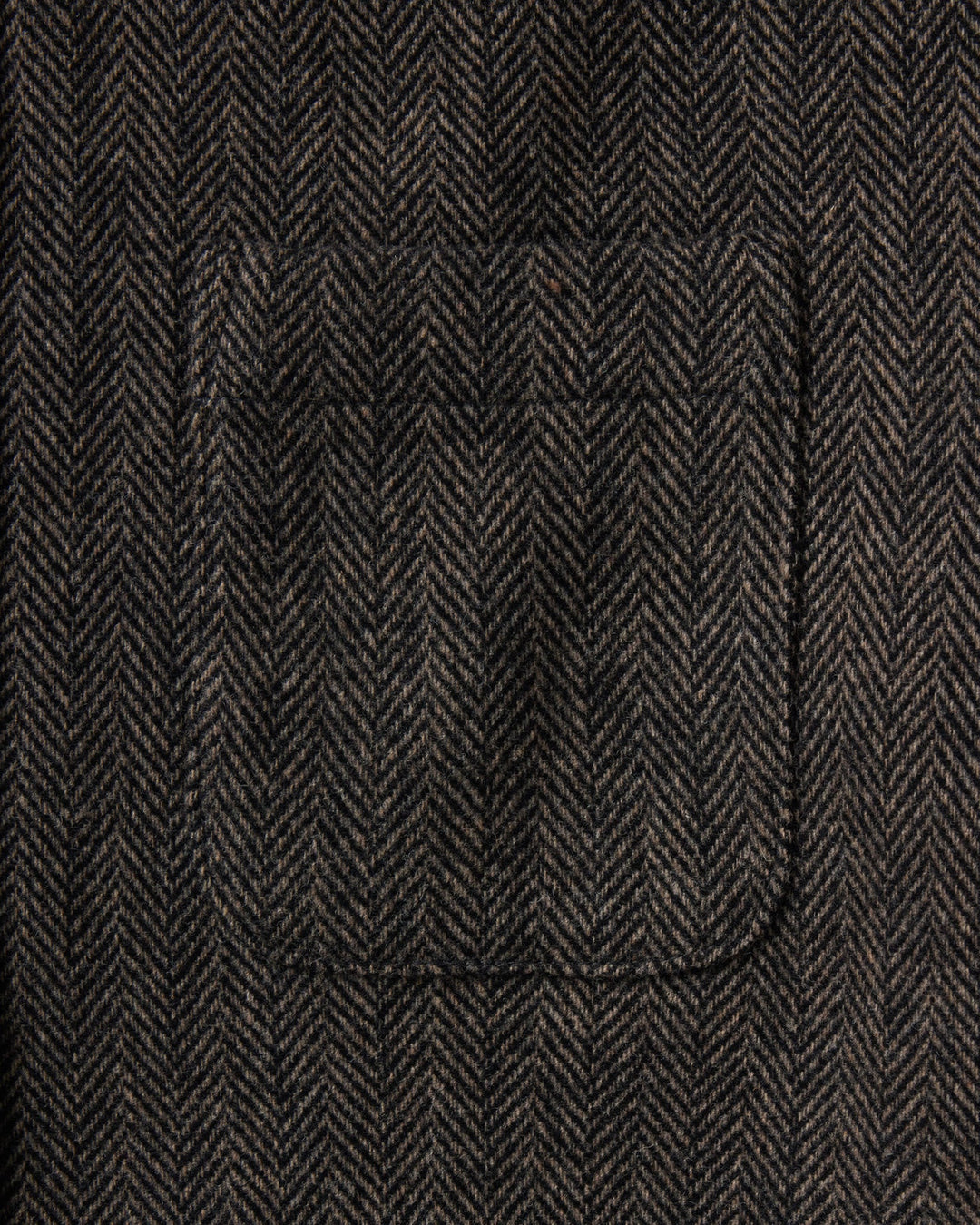 Close-up of a dark brown and black herringbone tweed fabric with a single welt pocket.