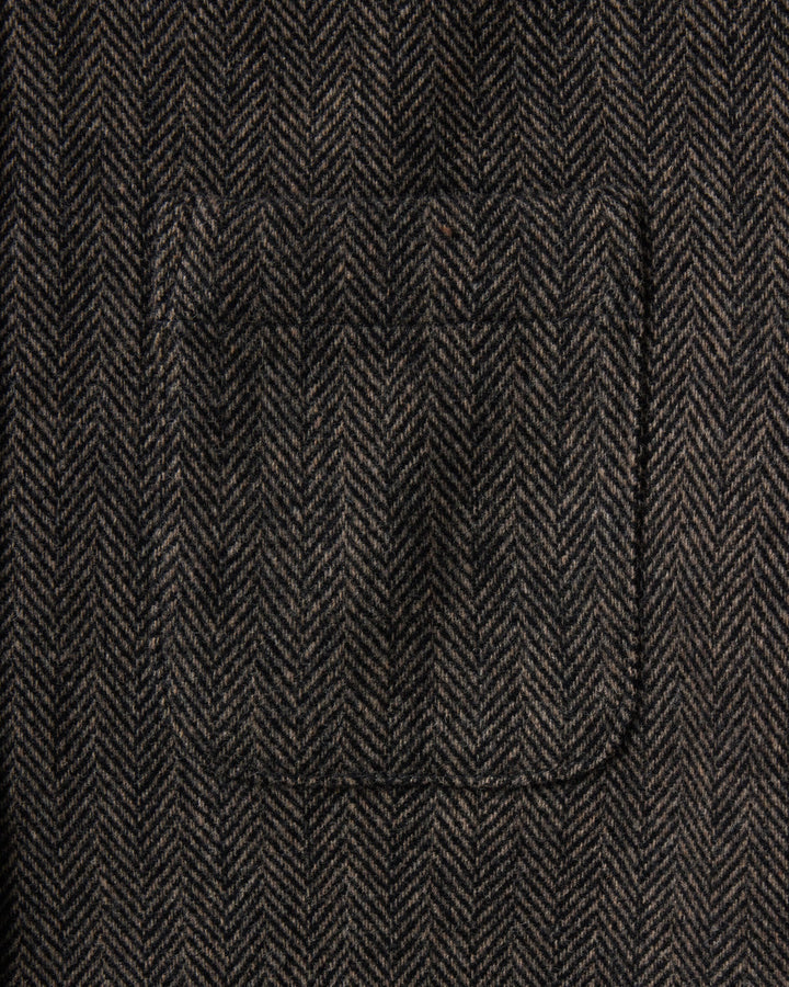 Close-up of a dark brown and black herringbone tweed fabric with a single welt pocket.