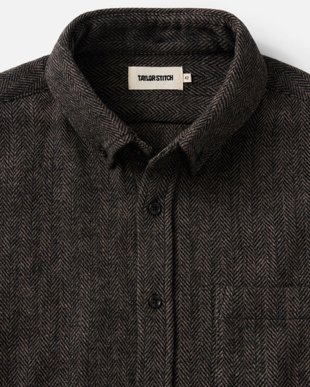 Close-up of a dark brown and black herringbone patterned button-down shirt by Taylor Stitch, showing the collar and front buttons.