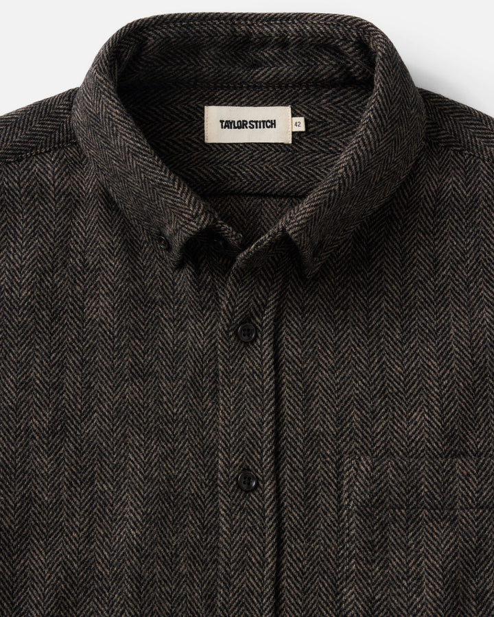 Close-up of a dark brown and black herringbone patterned button-down shirt by Taylor Stitch, showing the collar and front buttons.