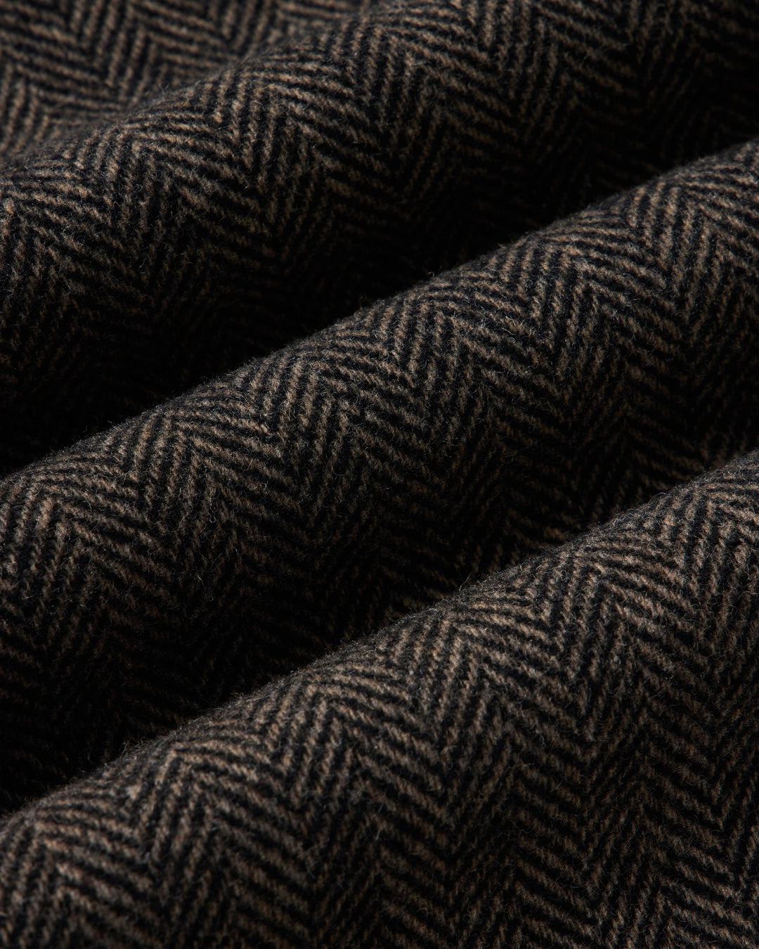 A close-up of draped fabric with a dark brown and black herringbone pattern.