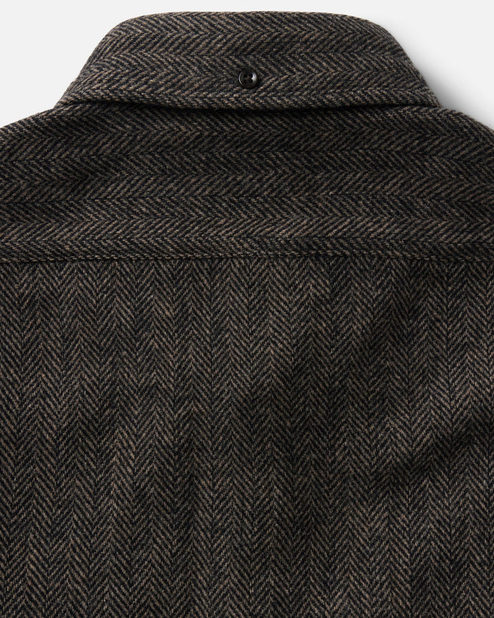 Close-up of the back of a dark brown and black herringbone tweed jacket, showing the collar, button, and detailed fabric weave.