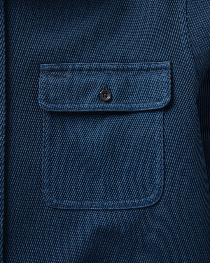 Close-up of a dark blue textured fabric garment featuring a single buttoned chest pocket with a flap.