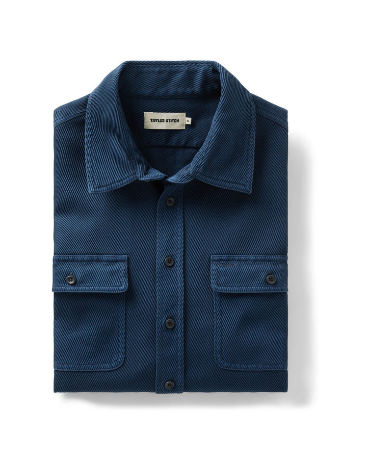 A folded navy blue textured button-down shirt with two chest flap pockets, displayed on a clean white background.