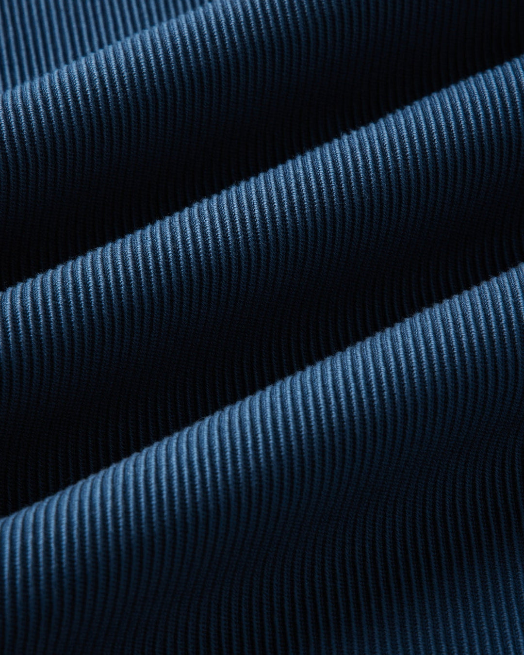 A close-up of dark blue ribbed fabric with a fine vertical stripe texture, shown in soft diagonal folds.