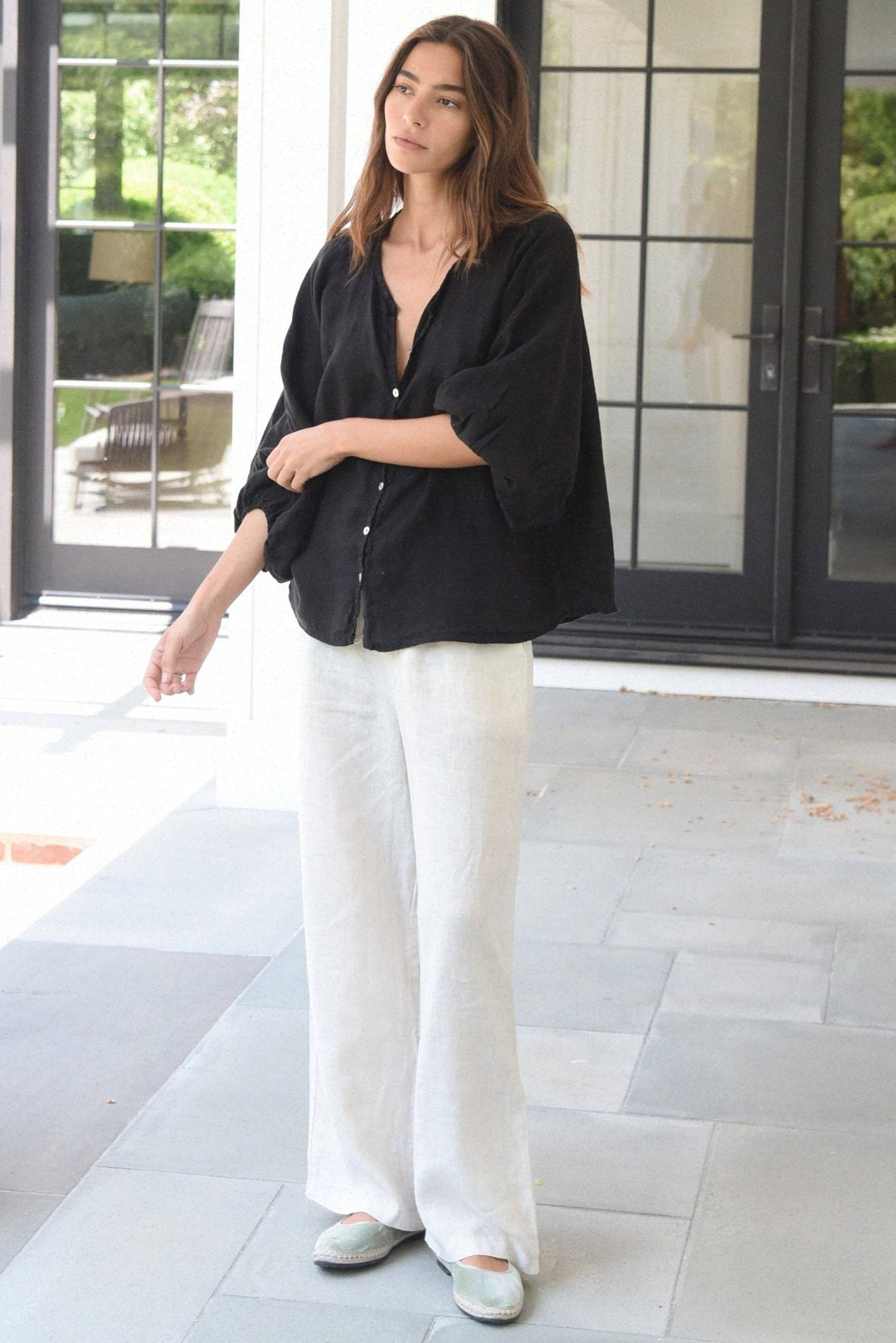 Woman wearing a black shirt and white pants standing on a tiled floor.