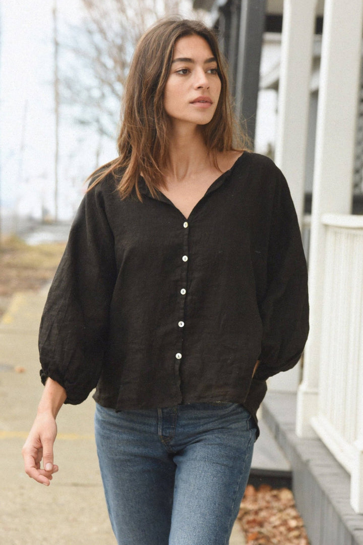Woman wearing a black button-up shirt and blue jeans walking outdoors.