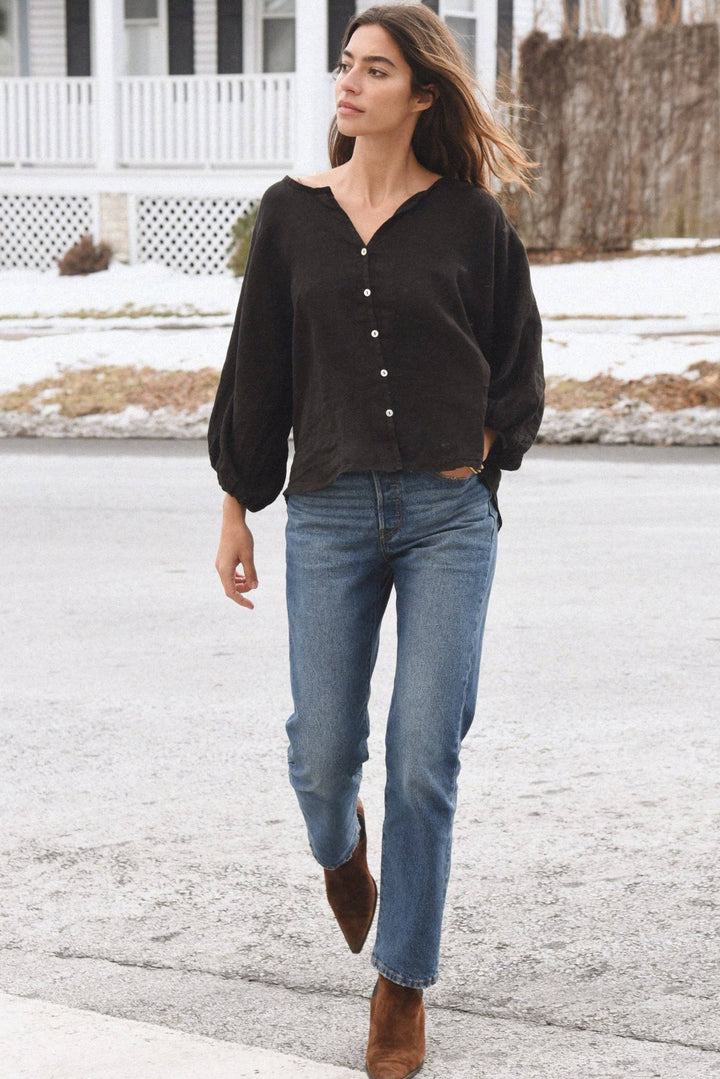 Woman walking outdoors in a residential area wearing a black top and blue jeans.