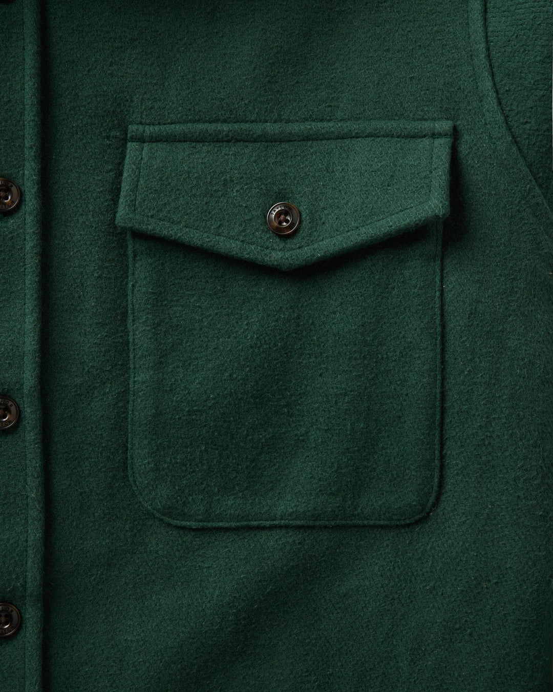Close-up of a dark forest green maritime shirt jacket featuring a single front chest pocket with a button flap and dark brown buttons.