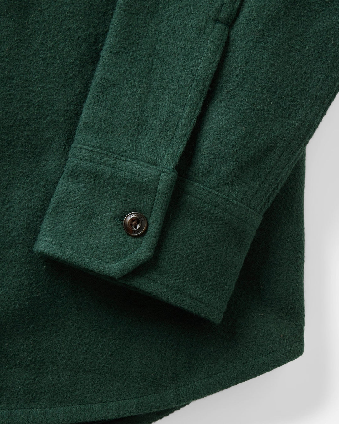 Close-up of a dark forest green maritime shirt jacket, showing the texture of the fabric and a single dark brown button on the cuff.