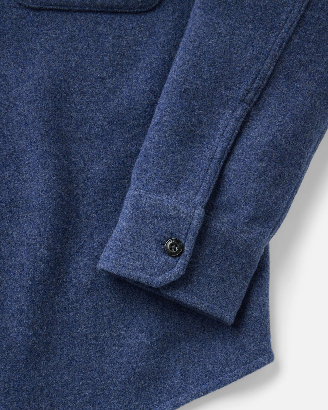 Close-up of The Maritime Shirt Jacket
in Heather Navy Wool, showing the fabric weave, a pocket, and a buttoned cuff on a light gray background.