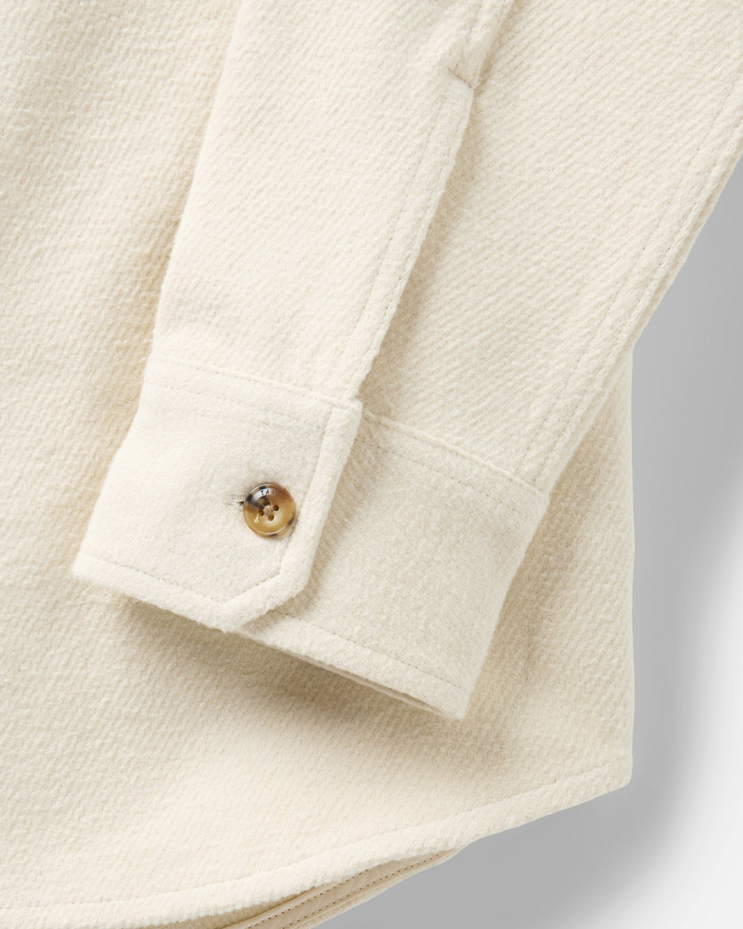 Close-up of a vintage white-colored textured fabric garment, showing a folded cuff with a single button.