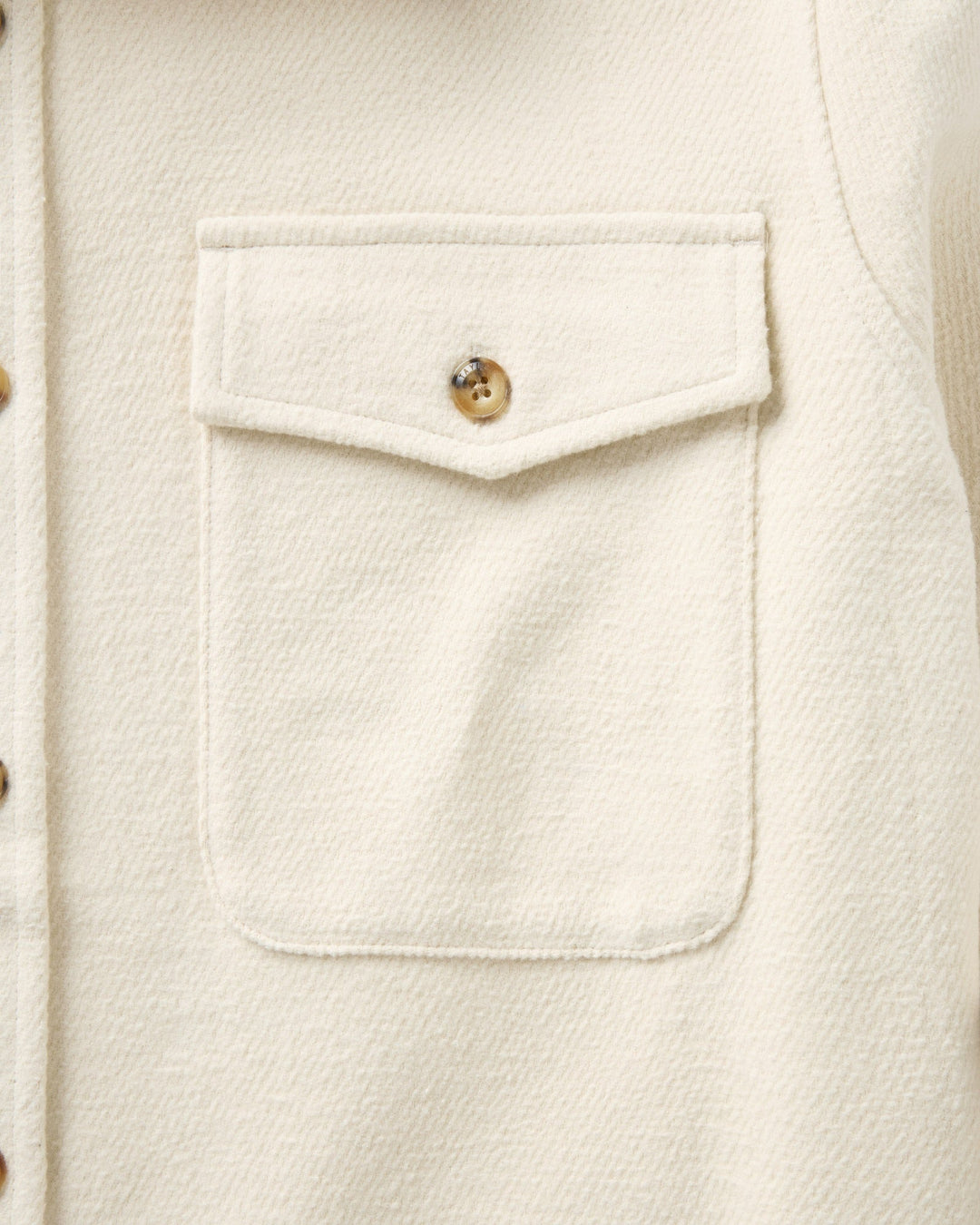 Close-up of a vintage-white textured fabric garment featuring a front chest pocket with a decorative flap and a single button.