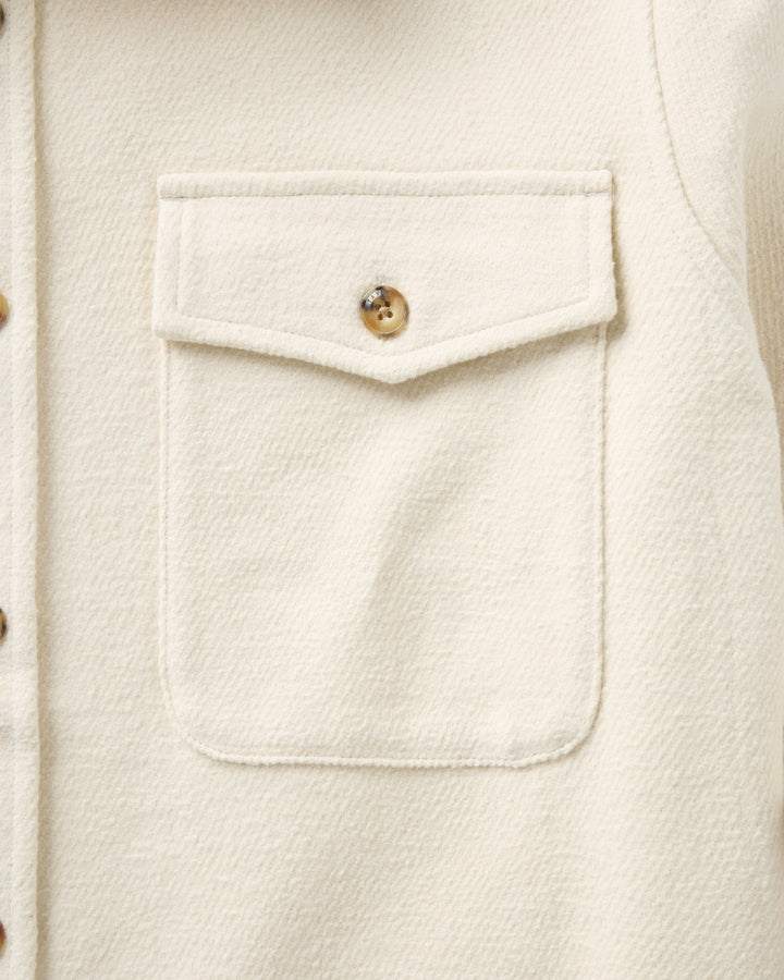 Close-up of a vintage-white textured fabric garment featuring a front chest pocket with a decorative flap and a single button.