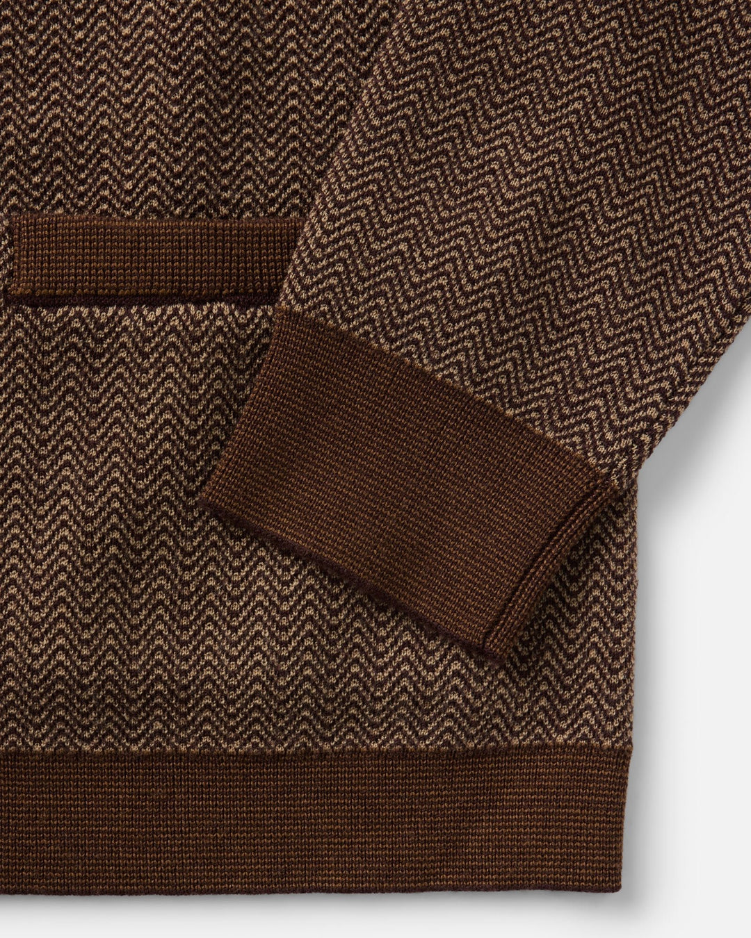 Close-up of The Miles Sweater Polo in Espresso Merino with a herringbone pattern and ribbed cuffs and hem, shown on a light gray background.