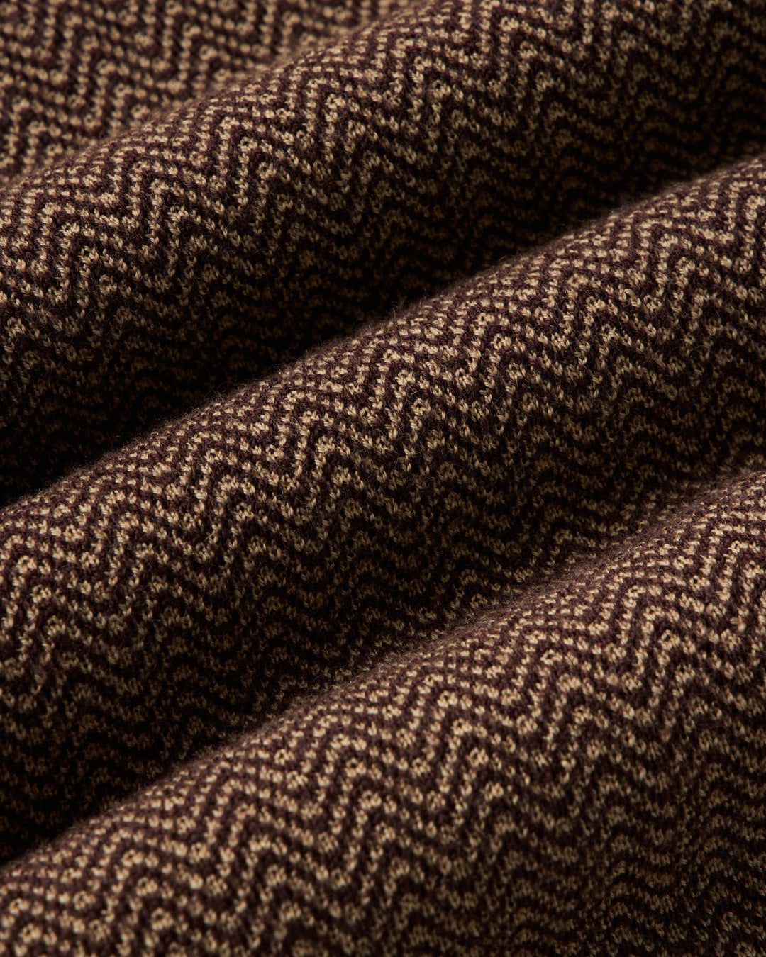 A close-up of a brown and beige herringbone woven fabric with a textured chevron pattern, shown in soft folds.