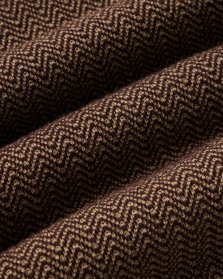 A close-up of a brown and beige herringbone woven fabric with a textured chevron pattern, shown in soft folds.