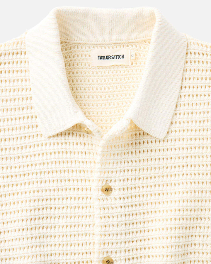 Close-up of The Monterey Sweater Polo in Vintage White Crochet and brand label on a light gray background