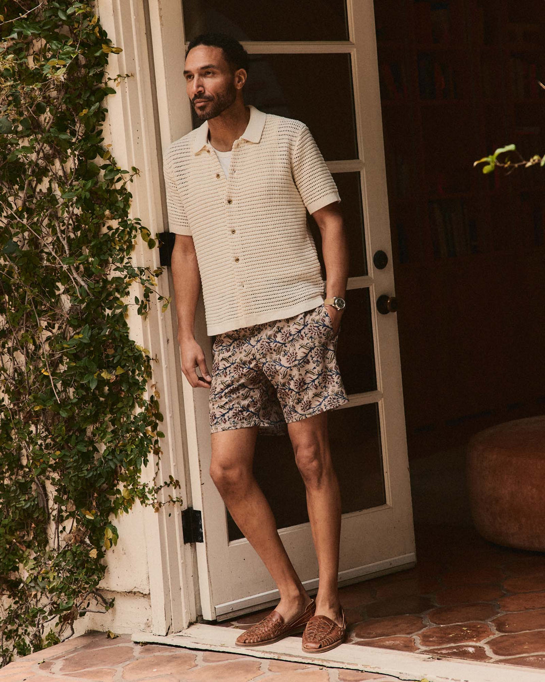 Man standing in front of a door wearing The Monterey Sweater Polo in Vintage White Crochet and shorts.