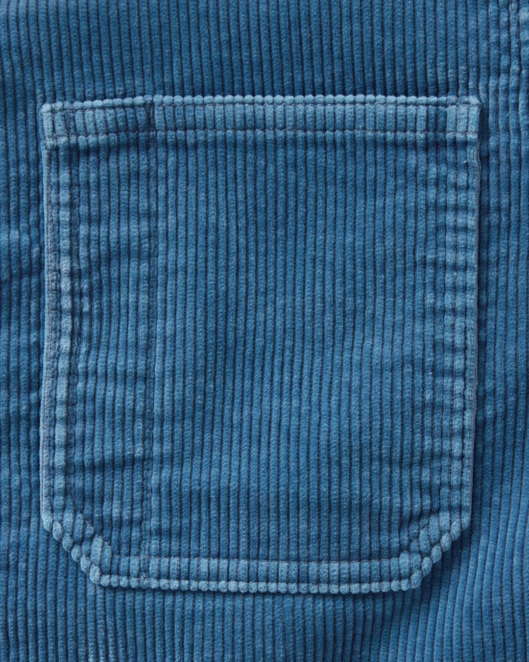 Close-up of a washed indigo corduroy fabric pocket with visible ribbed texture and stitched edges.