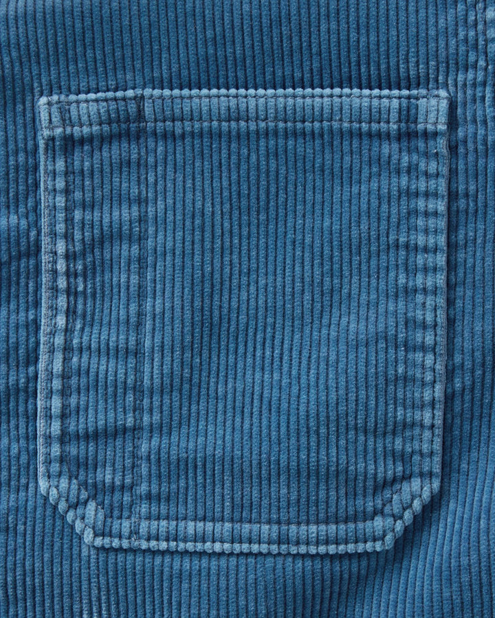 Close-up of a washed indigo corduroy fabric pocket with visible ribbed texture and stitched edges.