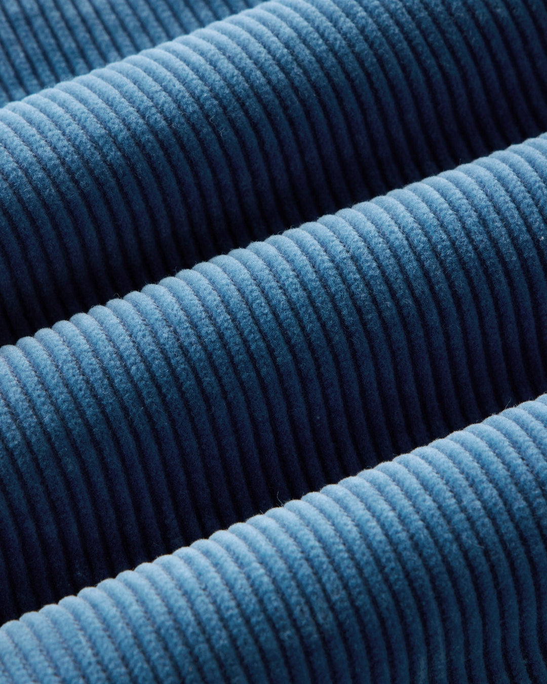 A close-up of washed indigo ribbed fabric with a textured corduroy-like surface, filling the entire frame.