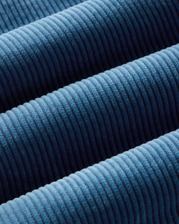 A close-up of washed indigo ribbed fabric with a textured corduroy-like surface, filling the entire frame.
