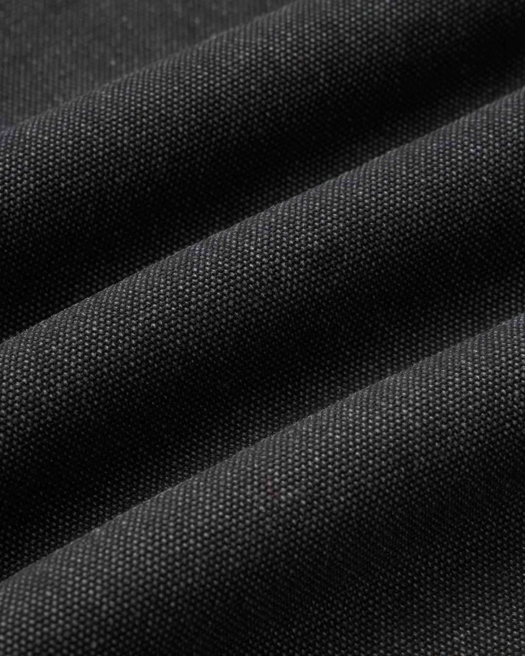 A close-up of dark charcoal gray fabric with a fine woven texture, shown in soft diagonal folds.