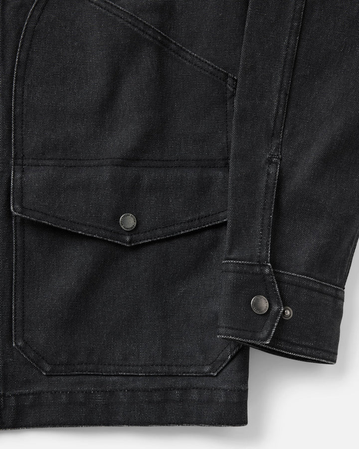 Close-up of a dark charcoal gray jacket, showing a flap pocket with a metal snap button and the cuff with a button closure.