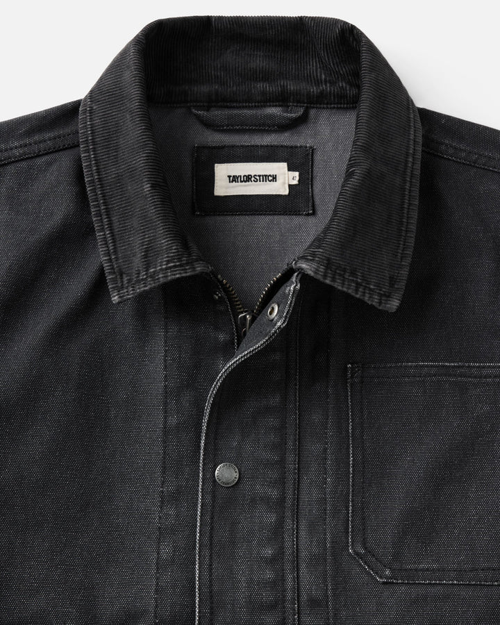 Close-up of a dark charcoal corduroy collar canvas jacket with a pointed collar, a visible neck label reading &