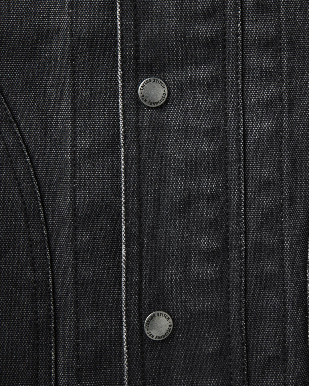 Close-up of a dark charcoal gray textured jacket or overshirt with vertical channel stitching and two round metal snap buttons.