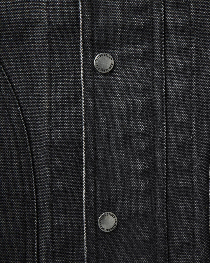 Close-up of a dark charcoal gray textured jacket or overshirt with vertical channel stitching and two round metal snap buttons.
