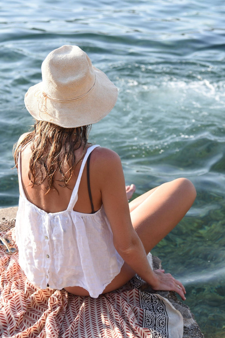 Woman sitting by the water wearing a white hat and white top.