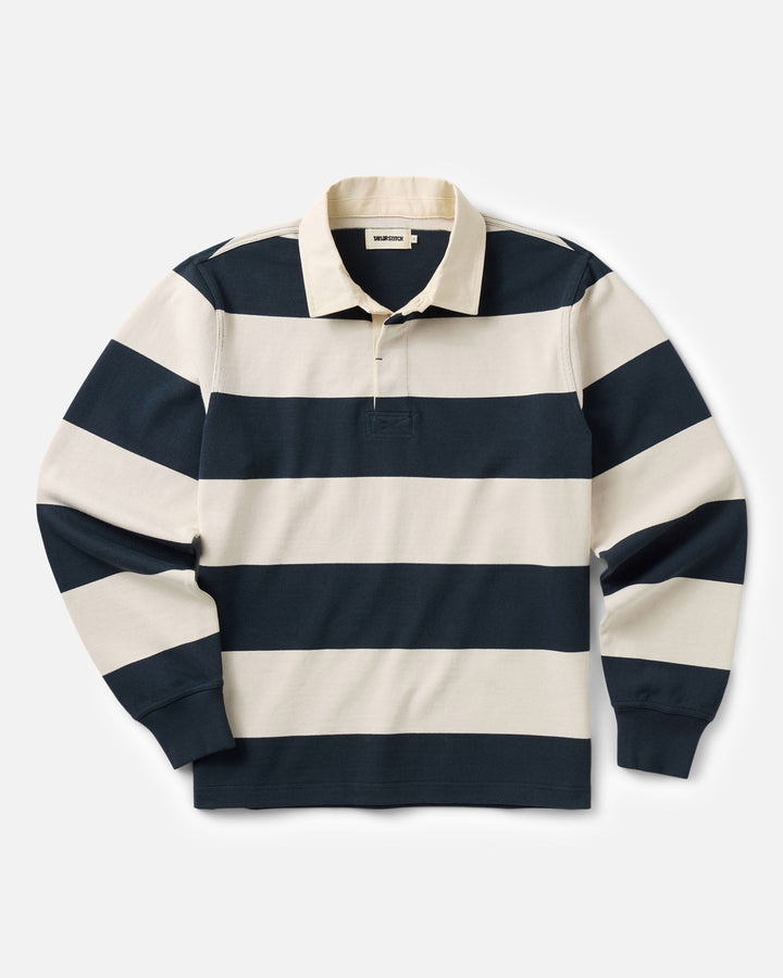 A long-sleeve rugby shirt with horizontal navy blue and cream stripes, featuring a classic collar and a three-button placket, laid flat against a light gray background.