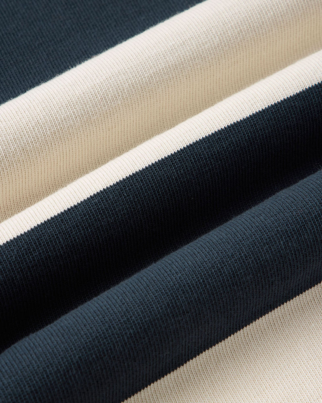 A close-up of striped knit fabric with alternating wide bands of dark navy and warm off-white/cream.