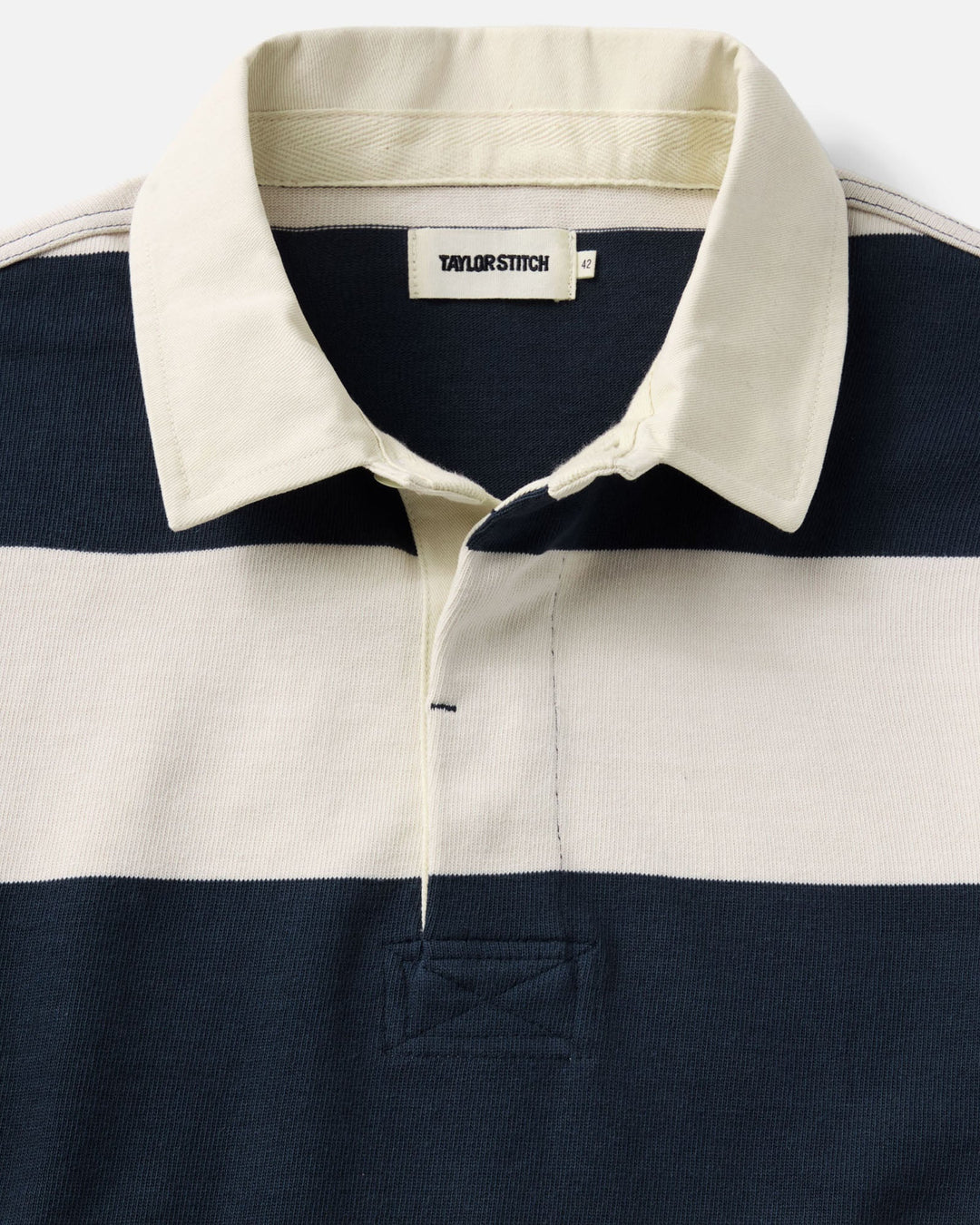Close-up of a striped rugby shirt by Taylor Stitch, featuring navy blue and cream horizontal stripes with a cream collar and button placket.
