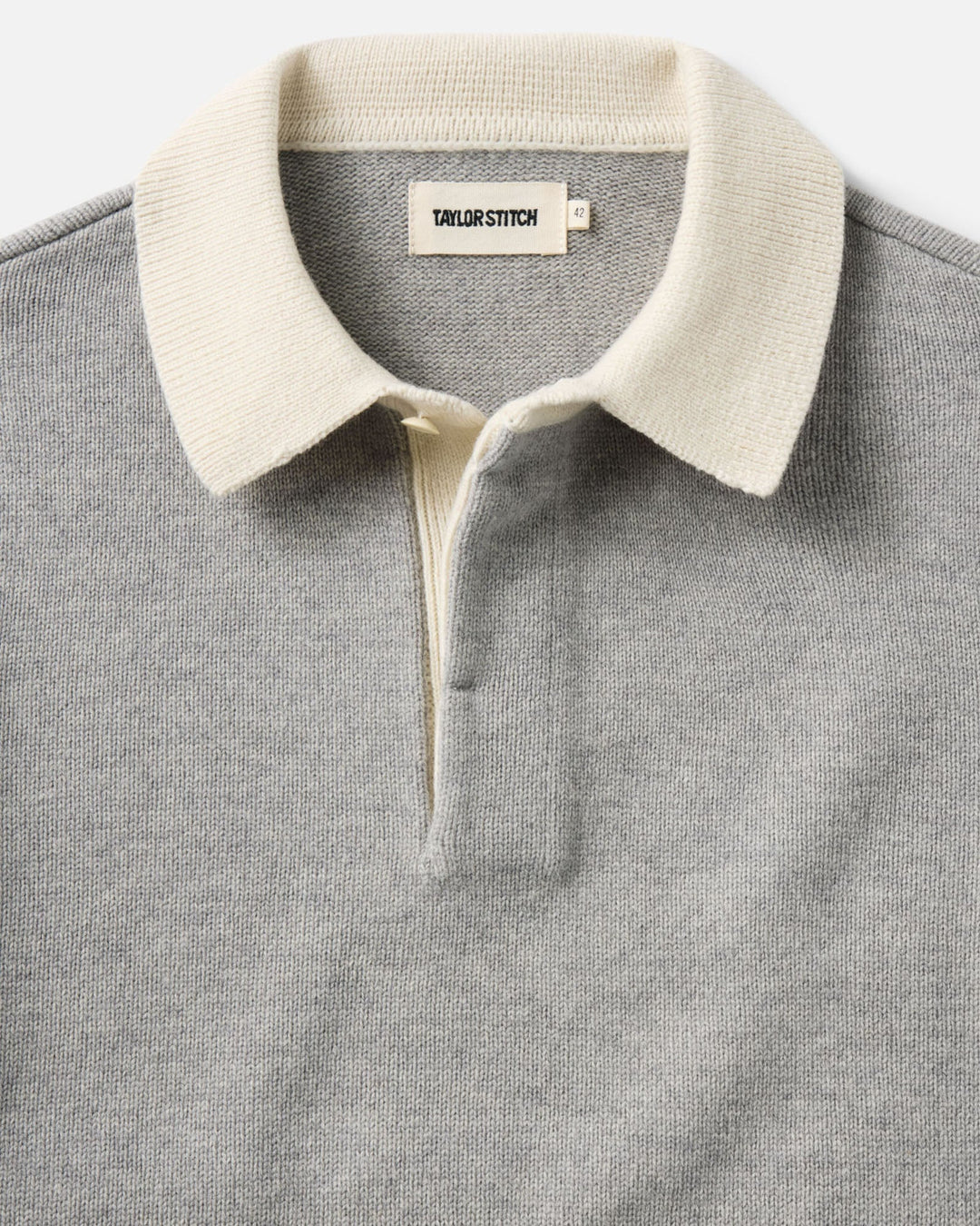 Close-up of a gray knit rugby shirt with a contrasting cream collar and placket, featuring a visible Taylor Stitch brand label.