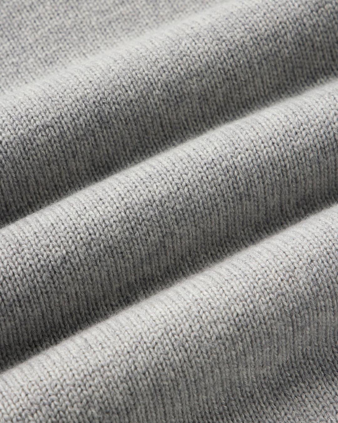 Close-up of a light gray ribbed knit fabric with soft diagonal folds showing the texture and weave.