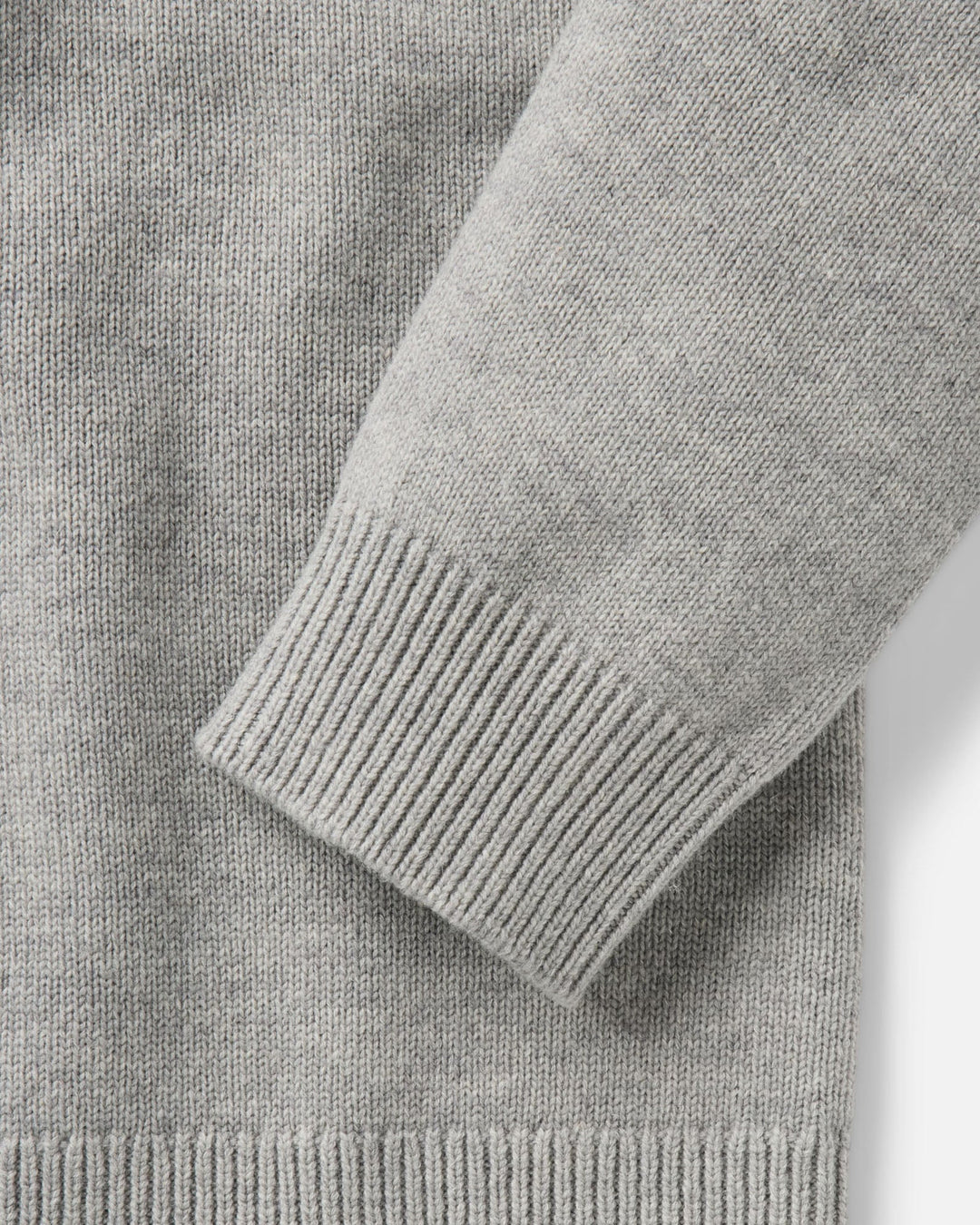 Close-up of a light gray knit sweater showing the ribbed cuff and sleeve construction.