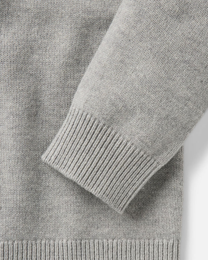 Close-up of a light gray knit sweater showing the ribbed cuff and sleeve construction.