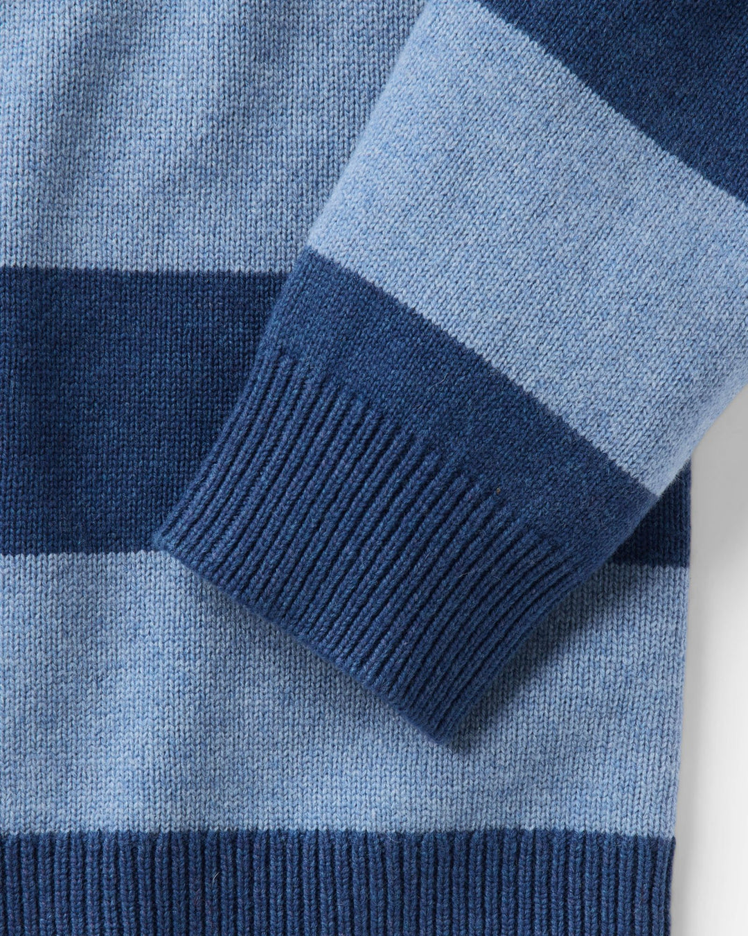 Close-up of a striped knit sweater, with horizontal bands in light blue, medium blue, and dark navy ribbed cuffs.