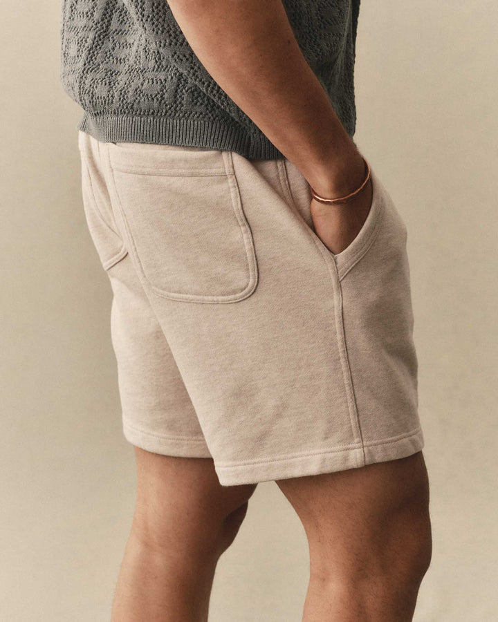 Man wearing Taylor Stitch Sunset Shorts in Heather Oat Terry and a dark knitted shirt on a neutral background
