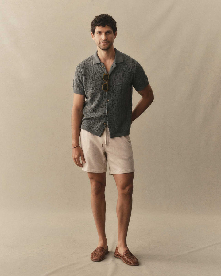 Man wearing Taylor Stitch Sunset Shorts in Heather Oat Terry and a dark knitted shirt on a neutral background